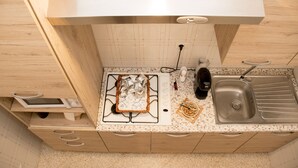 Una cocina compacta con estufa a gas, lavamanos y alacenas de madera.