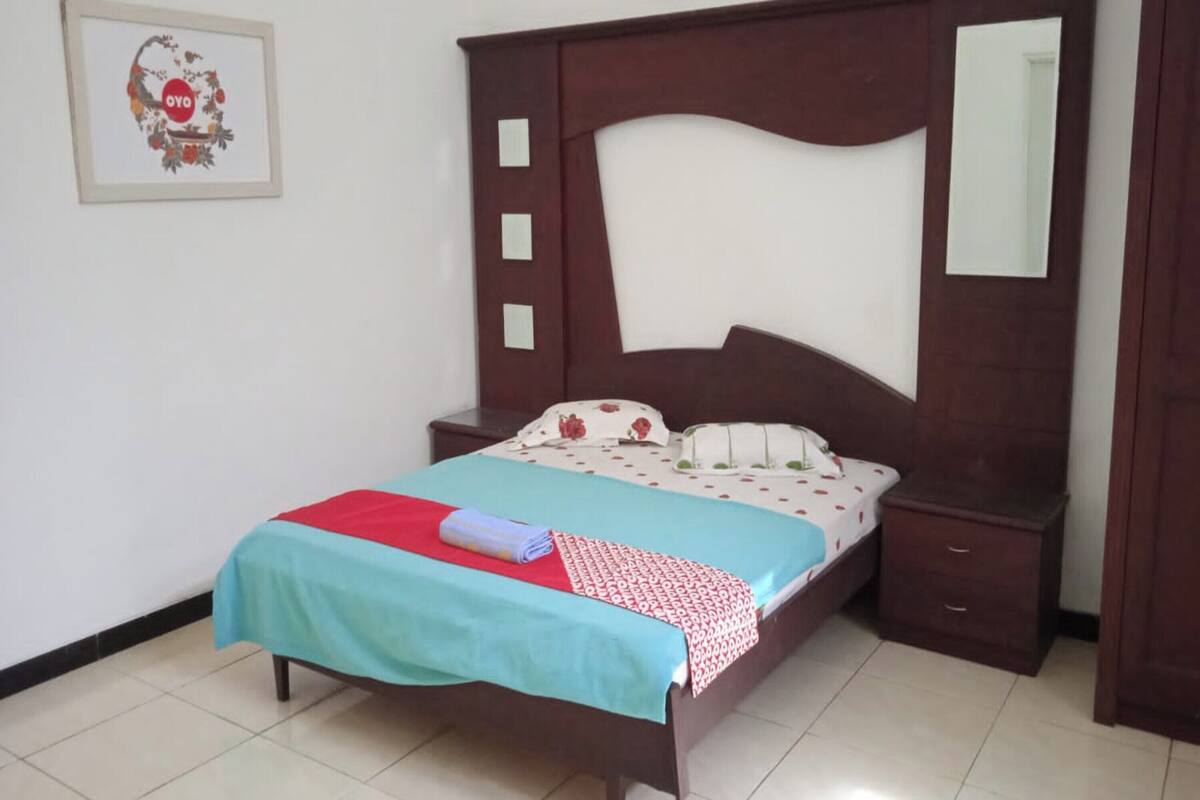 Une chambre à coucher comprenant un lit, une table de chevet, une commode, un miroir et un tableau encadré accroché au mur.