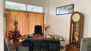 Une pièce comprenant un bureau, une chaise, une grande horloge et une fenêtre avec des rideaux.