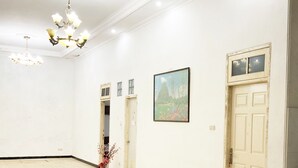 Une pièce spacieuse, ornée d’un grand lustre, avec une porte dotée d’une fenêtre et un tableau représentant un paysage, encadré et accroché au mur.