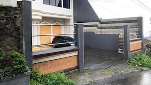 Un bâtiment moderne avec un mur en pierre, une voiture noire garée devant et une entrée fermée par un portail.