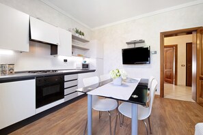 A modern kitchen with white cabinets, a black countertop, and a dining area with a glass table and white chairs.