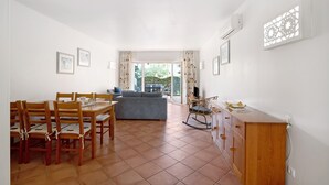 A dining area with wooden chairs and a table, a sofa, and a view through a glass door to an outdoor area. - Apartment 'Tavirasol' with Shared Pool, Wi-Fi and Air Conditioning (Tavira)