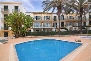 A swimming pool with a tiled edge, a palm tree, and a building with balconies and windows.