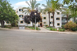 A multi-story building with balconies, palm trees, and a paved entrance area.