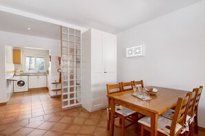 A kitchen with a washing machine, a dining table with chairs, and a white cabinet.
