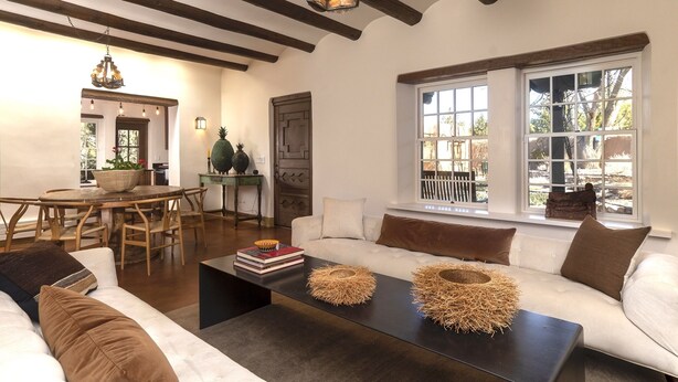 Amplia sala de estar con una mesa de comedor de madera, sofás blancos y un gran ventanal con vistas al exterior.