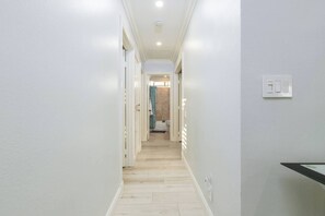 A narrow hallway with light-colored walls and wooden flooring, leading to a bathroom with a bathtub and toilet. - Extended Stay Oasis w/ yard & Arcade (Maple Perch) (Mission Viejo)