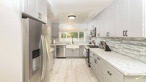 Una cocina moderna con armarios blancos, un refrigerador de acero inoxidable, un lavavajillas y un salpicadero de azulejos.