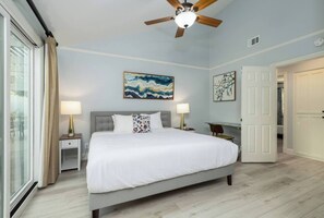 Une chambre à coucher avec un grand lit, deux tables de chevet avec des lampes, un ventilateur de plafond et des œuvres d’art accrochées aux murs.
