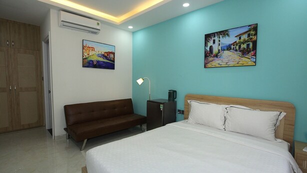 Una habitación de hotel con cama, sofá, equipo de aire acondicionado y dos cuadros en las paredes.