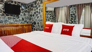 A hotel room with a stone wall, a wooden bed frame, a flat-screen TV, and a clock.