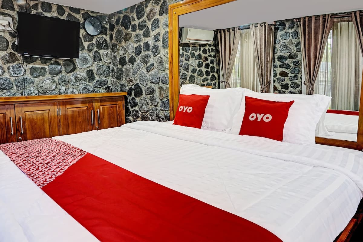 A hotel room with a stone wall, a wooden bed frame, a flat-screen TV, and a clock.
