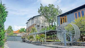 A paved courtyard with a large metal sculpture, a stone wall, and a building with a blue facade and wooden doors.