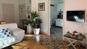 Un salon comprenant un canapé, une table basse, une grande plante en pot et un téléviseur fixé au mur.