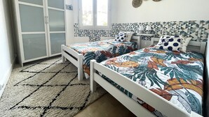 Une chambre avec deux lits, une armoire, une fenêtre et un mur décoré d’assiettes.