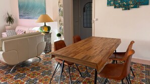 Un coin repas avec une table et des chaises en bois, un sol à motifs, un canapé, une lampe et un tableau représentant une vague accroché au mur.