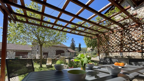 Un patio al aire libre con una pérgola, paredes de piedra y vista a una casa de piedra.