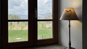 Habitación con un ventanal grande que ofrece vistas a un área verde y árboles. Hay una lámpara con un diseño de corazón en la pantalla.