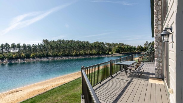 A deck with a table and chairs overlooking a lake and beach.