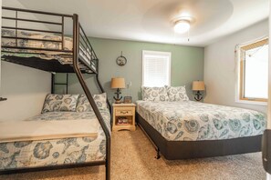 A bedroom with bunk beds, a small bedside table with lamps, a clock, and a window with blinds.