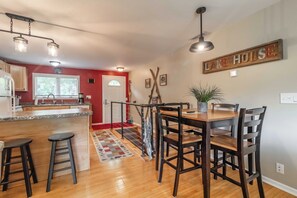 A kitchen with a wooden island, bar stools, a dining table with chairs, and a 'Lake House' sign on the wall.