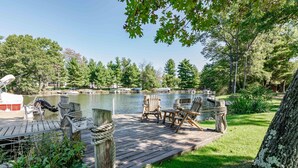 A wooden dock with chairs and tables, a caution sign, and a lake with boats and trees in the background. - LOVELY LAKEFRONT HOME ON THE EASTERN SIDE OF CASTLE ROCK LAKE (Friendship)