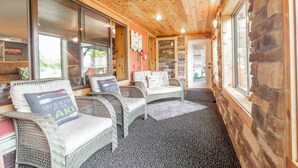 A cozy indoor seating area with wicker furniture, a stone wall, and large windows. - LOVELY LAKEFRONT HOME ON THE EASTERN SIDE OF CASTLE ROCK LAKE (Friendship)