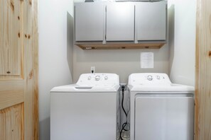 A laundry room with two white washing machines and a cabinet above.