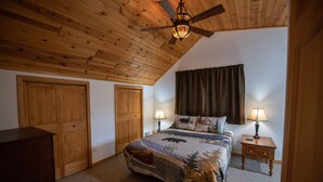 Un dormitorio con techo de madera, una cama con colcha de motivos forestales, dos lámparas de noche y una mesita de noche.