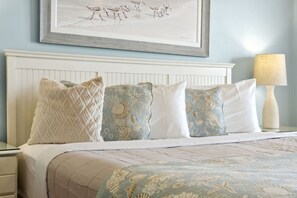 A bedroom with a bed, pillows, a nightstand, a lamp, and a framed artwork on the wall.