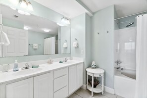A modern bathroom with a large mirror, two sinks, a toilet, and a shower.