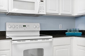 A kitchen with white cabinetry, a white stove, and a microwave above it. - Sunrise Resort Waterfront Beach and Pools Sleeps 8 (Panama City Beach)