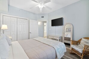 Une chambre à coucher comprenant un lit, une télévision, une commode, une chaise et un ventilateur de plafond.