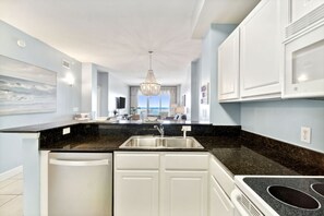 A modern kitchen with a black countertop, white cabinets, and a view to the outside. - Sunrise Resort Waterfront Beach and Pools Sleeps 8 (Panama City Beach)