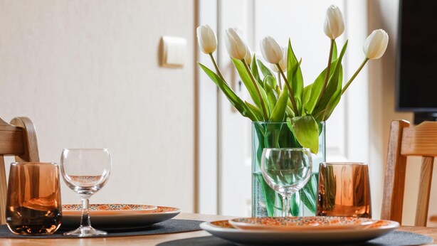 Una mesa de comedor con platos, vasos y un jarrón de tulipanes blancos.