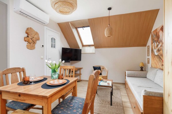 A compact living space with a dining area, a sofa, a TV, and a ceiling with a skylight.