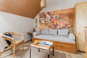 A cozy room with a wicker chair, a grey sofa, a wooden coffee table, and a wall-mounted shelf.