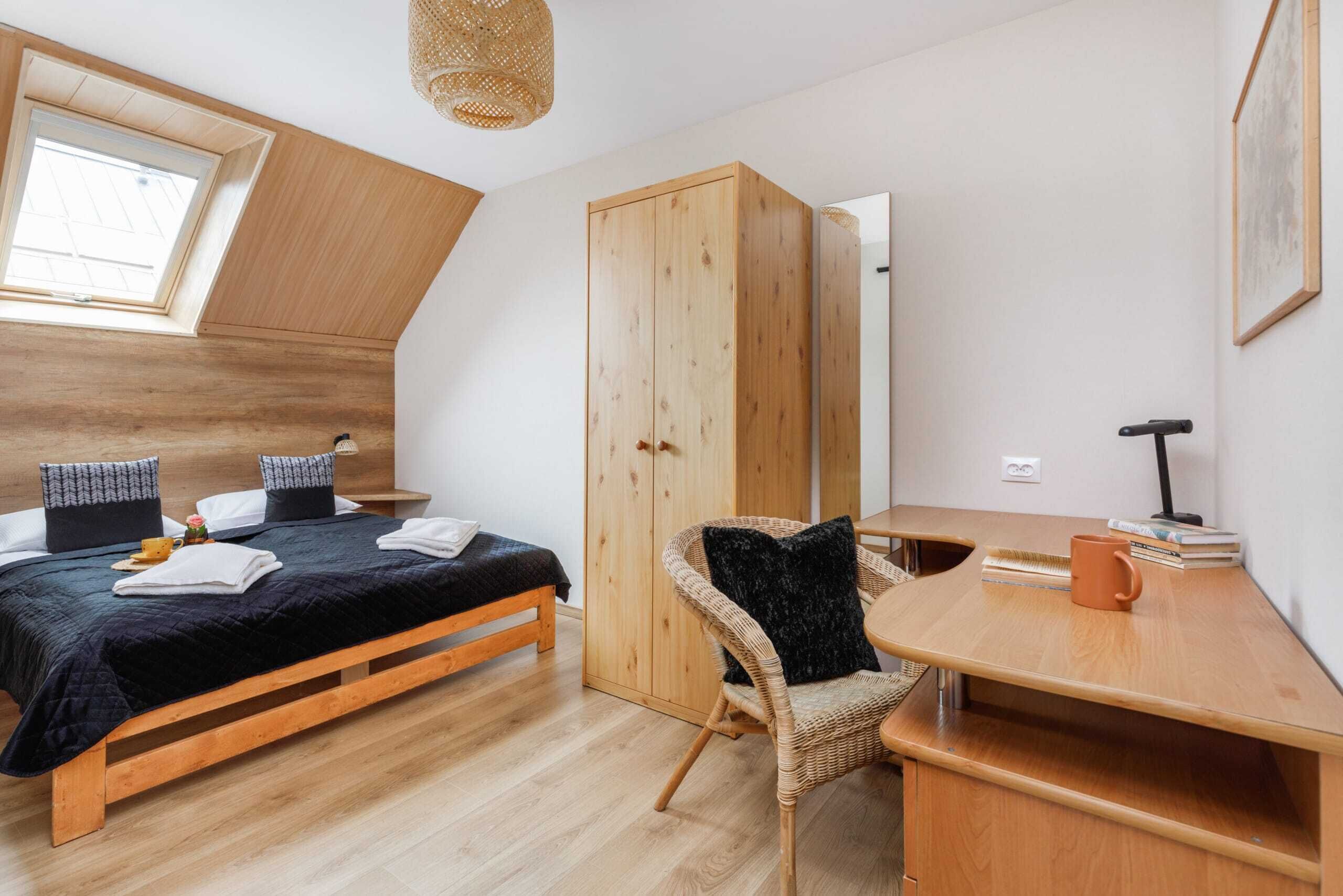 Een slaapkamer met een houten bed, een kledingkast, een stoel, een bureau en een raam.