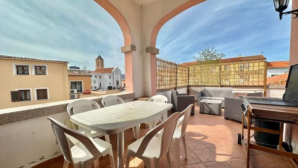 Eine Dachterrasse mit Tisch, Stühlen, einem Grill und Blick auf Gebäude und eine Kirche.