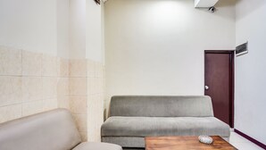 Een kleine, goed verlichte kamer met een beige bank, een grijze bank en een houten tafel met een decoratief object.