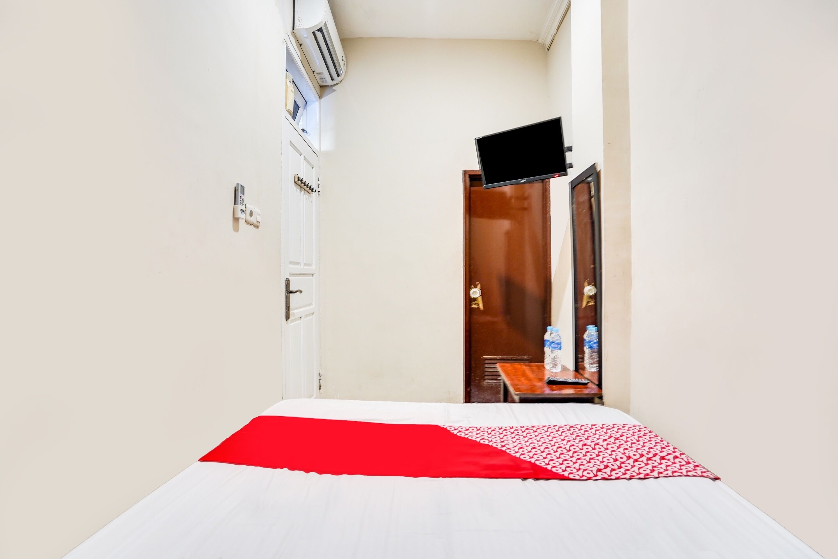 Habitación de hotel con cama, televisor de pantalla plana montado en la pared y puerta que da a un baño.