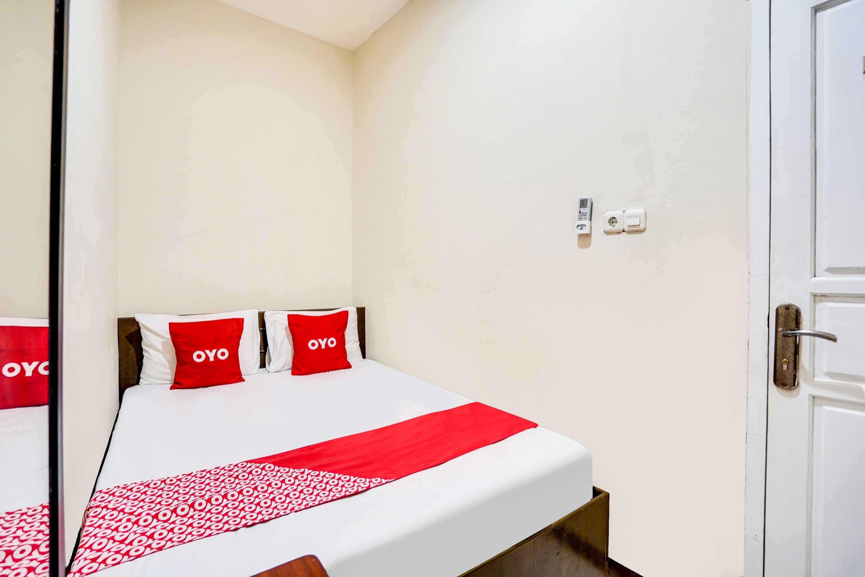 Une chambre d’hôtel avec un lit, des murs blancs et une couvre-lit à motifs rouges et blancs.
