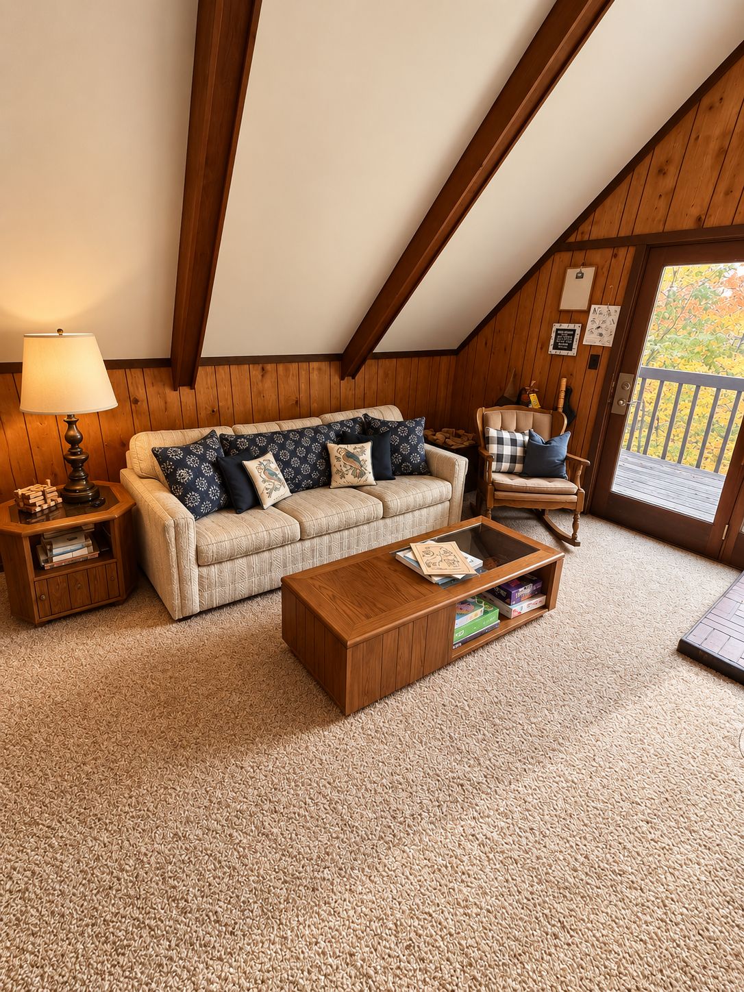 A cozy living room with a sofa, coffee table, and a chair. There is a lamp on a side table, and a door leading outside.