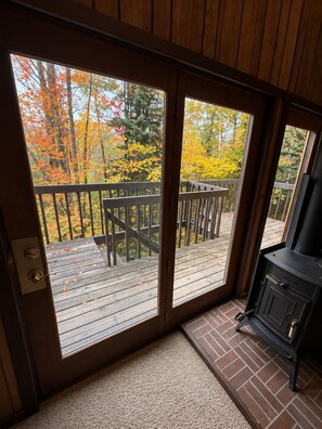 A wooden deck with a view of autumn foliage, a sliding glass door, and a black stove.