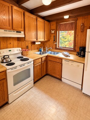 Une cuisine avec des meubles de rangement en bois, une cuisinière, un lave-vaisselle et une fenêtre donnant sur les arbres.