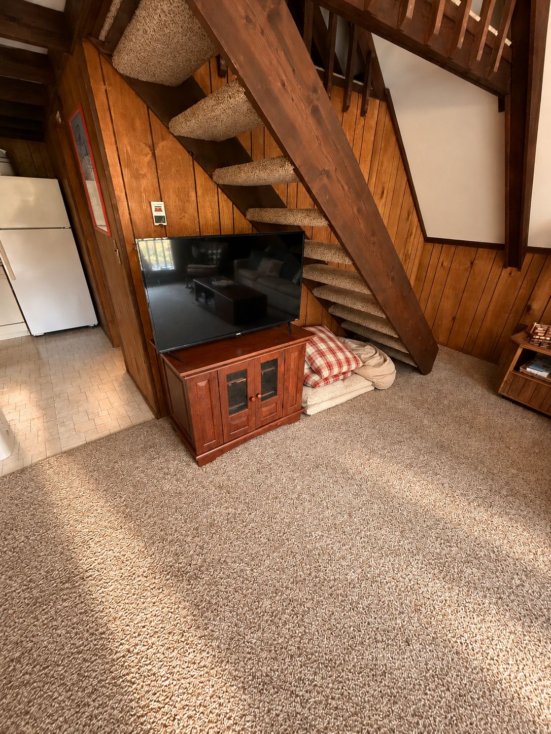 A wooden staircase with a television on a cabinet in a room with a carpeted floor.