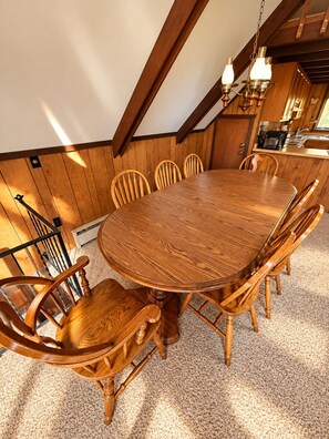 A wooden dining table with chairs, a chandelier, and a kitchen in the background. - Vacation Home in Quiet Wooded Setting with Beautiful Scenic Views from Living (Bessemer)