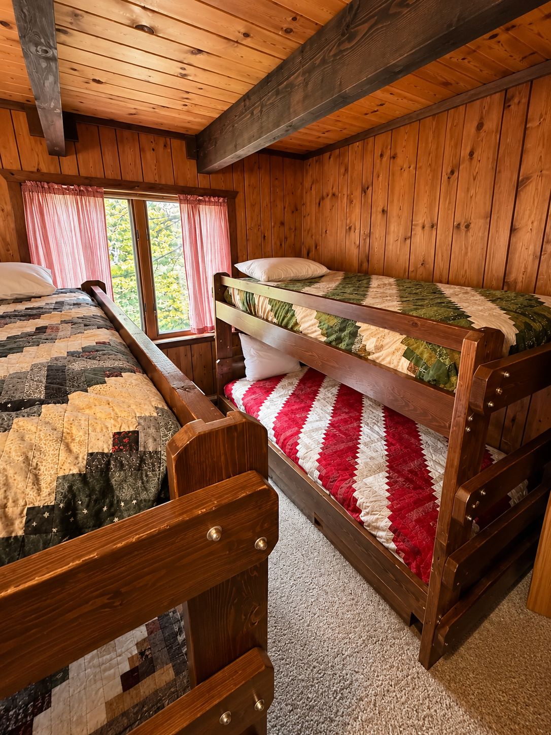 A cabin with two bunk beds, wooden walls, and a window with curtains.