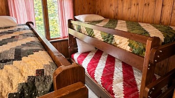 A cabin with two bunk beds, wooden walls, and a window with curtains.